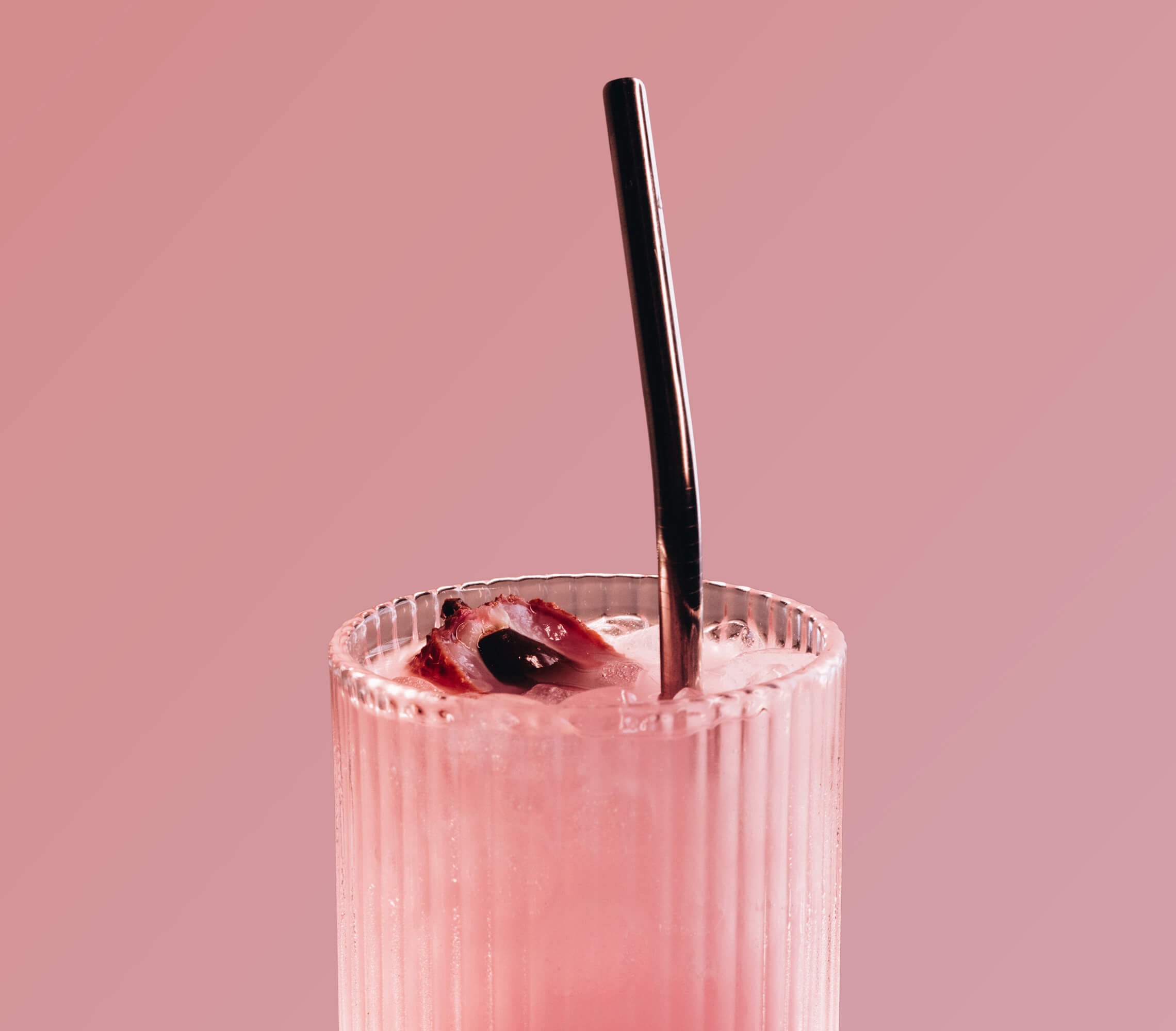 Pink cocktail with a metal straw against a pink background