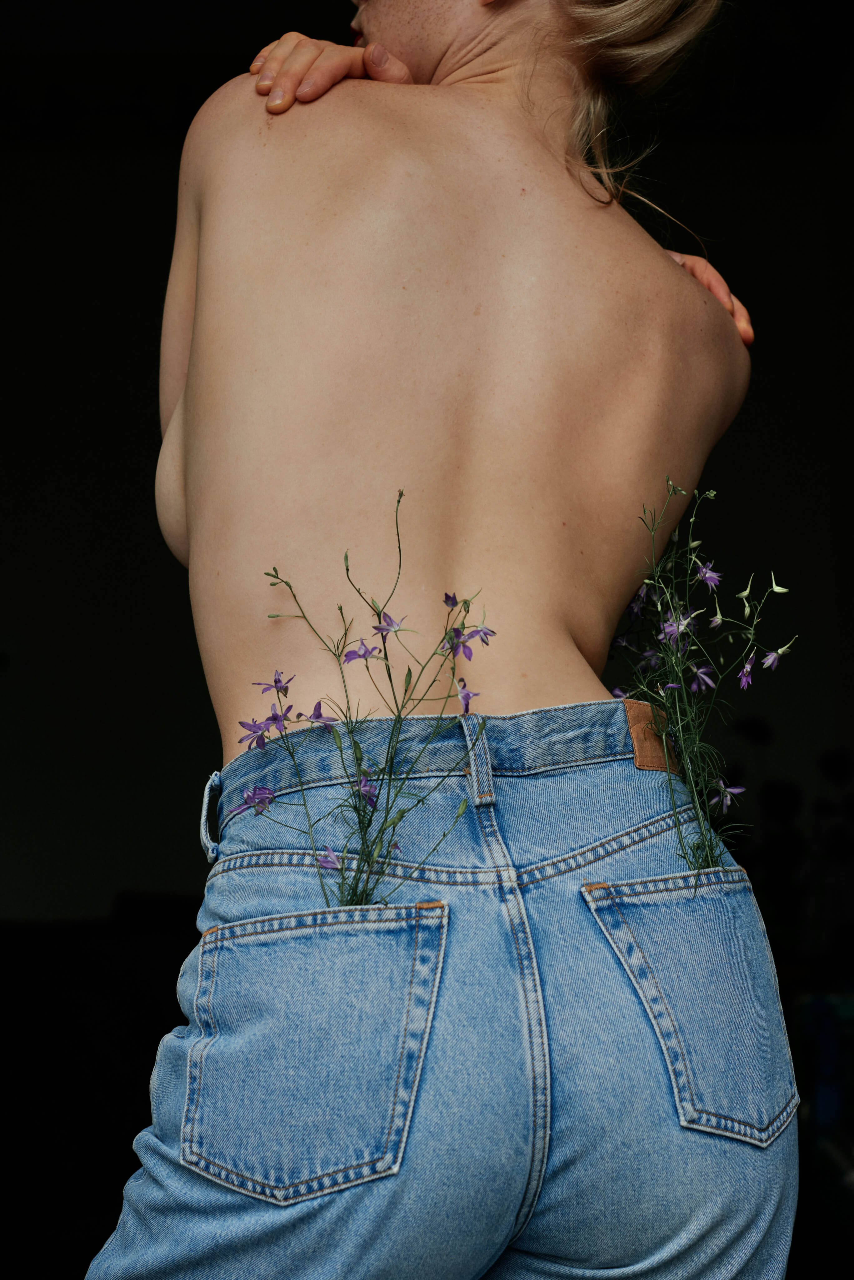Person wearing blue jeans with wildflowers in the pockets against a black background