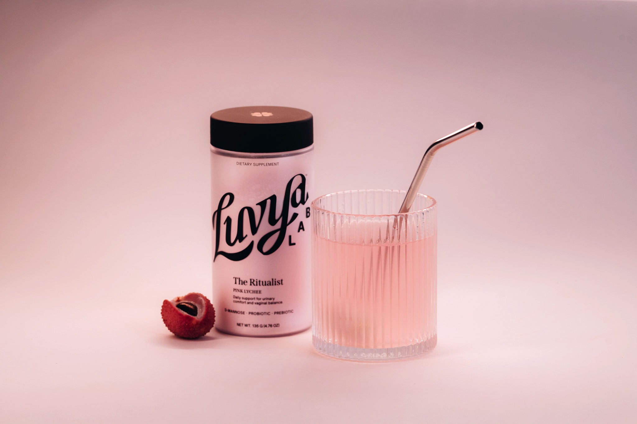The Ritualist jar beside a glass of Pink Lychee drink and fresh lychee