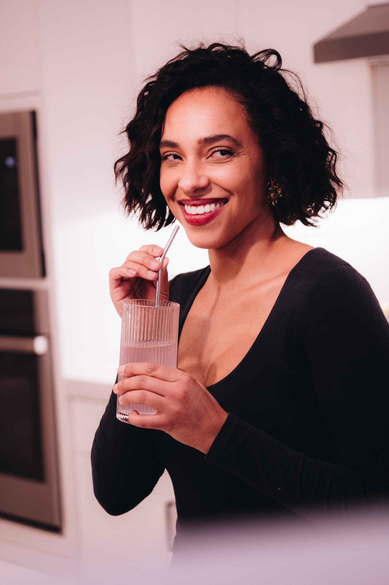 Brooke, the founder of Luvya Lab, smiling as she drinks a pale pink Luvya Lab drink through a straw