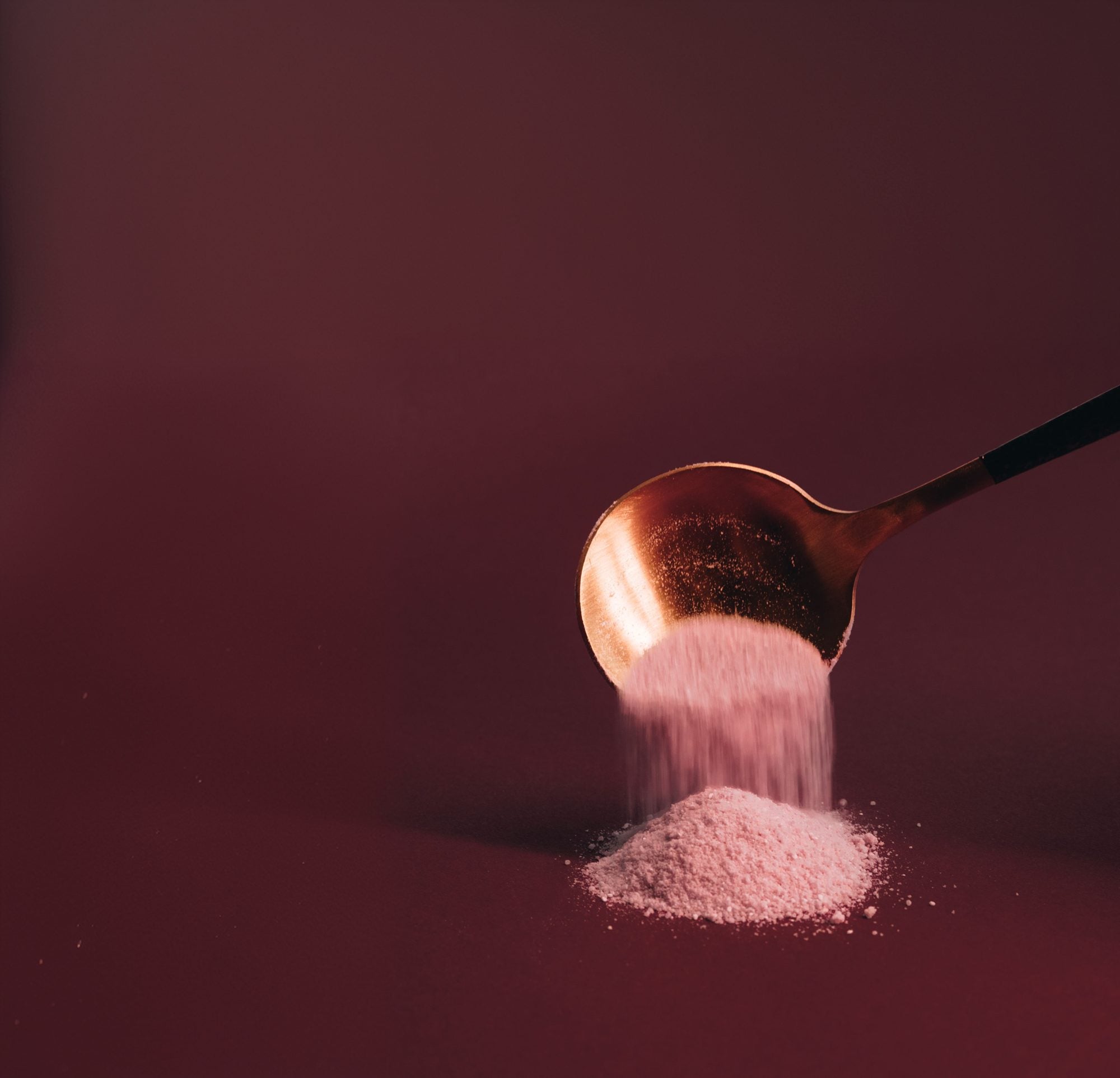 A wooden spoon tipping pink Luvya Lab powder into a mound beside the open jar